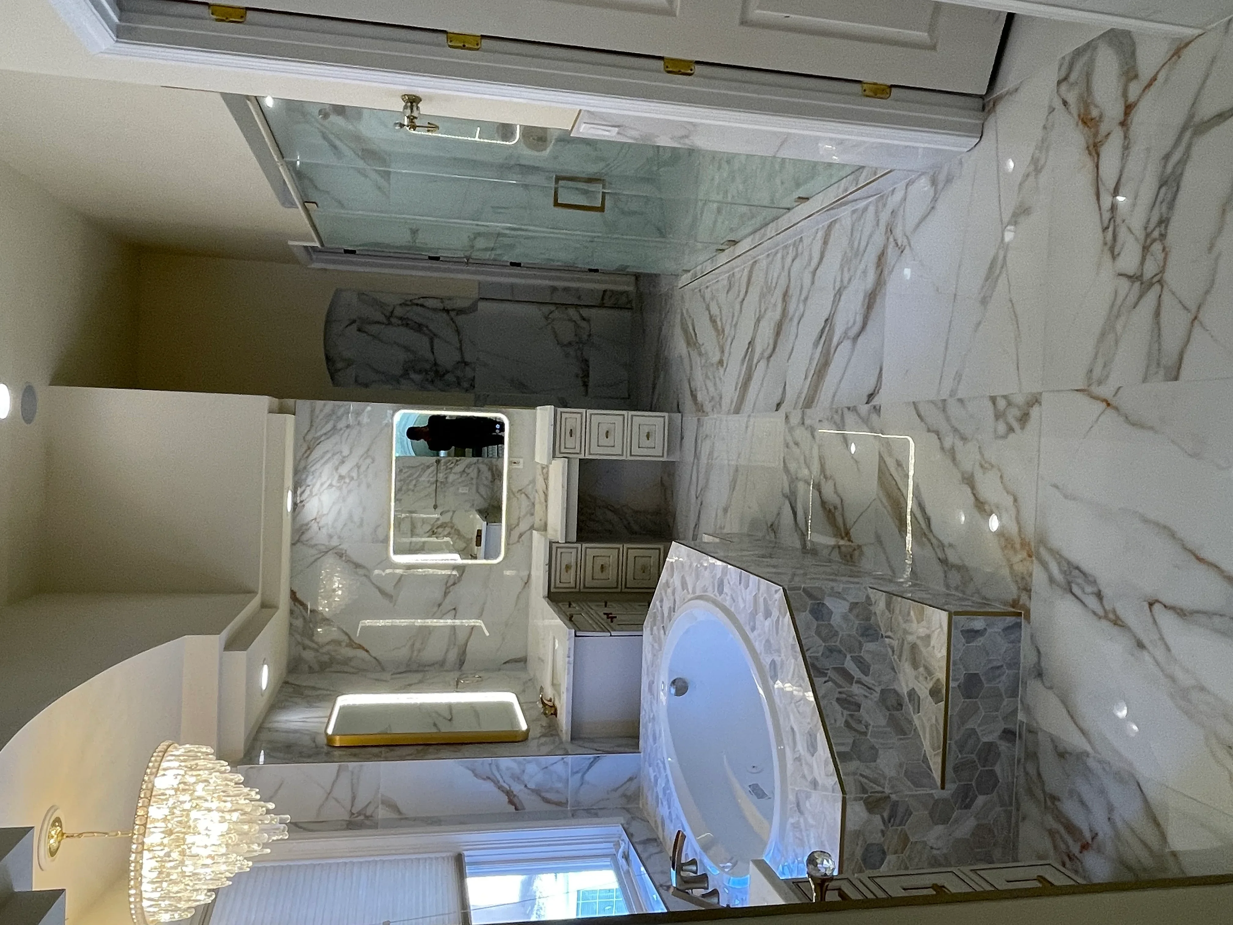 Overhead view of marble-tiled bathroom with glass shower, LED mirror, and white vanity