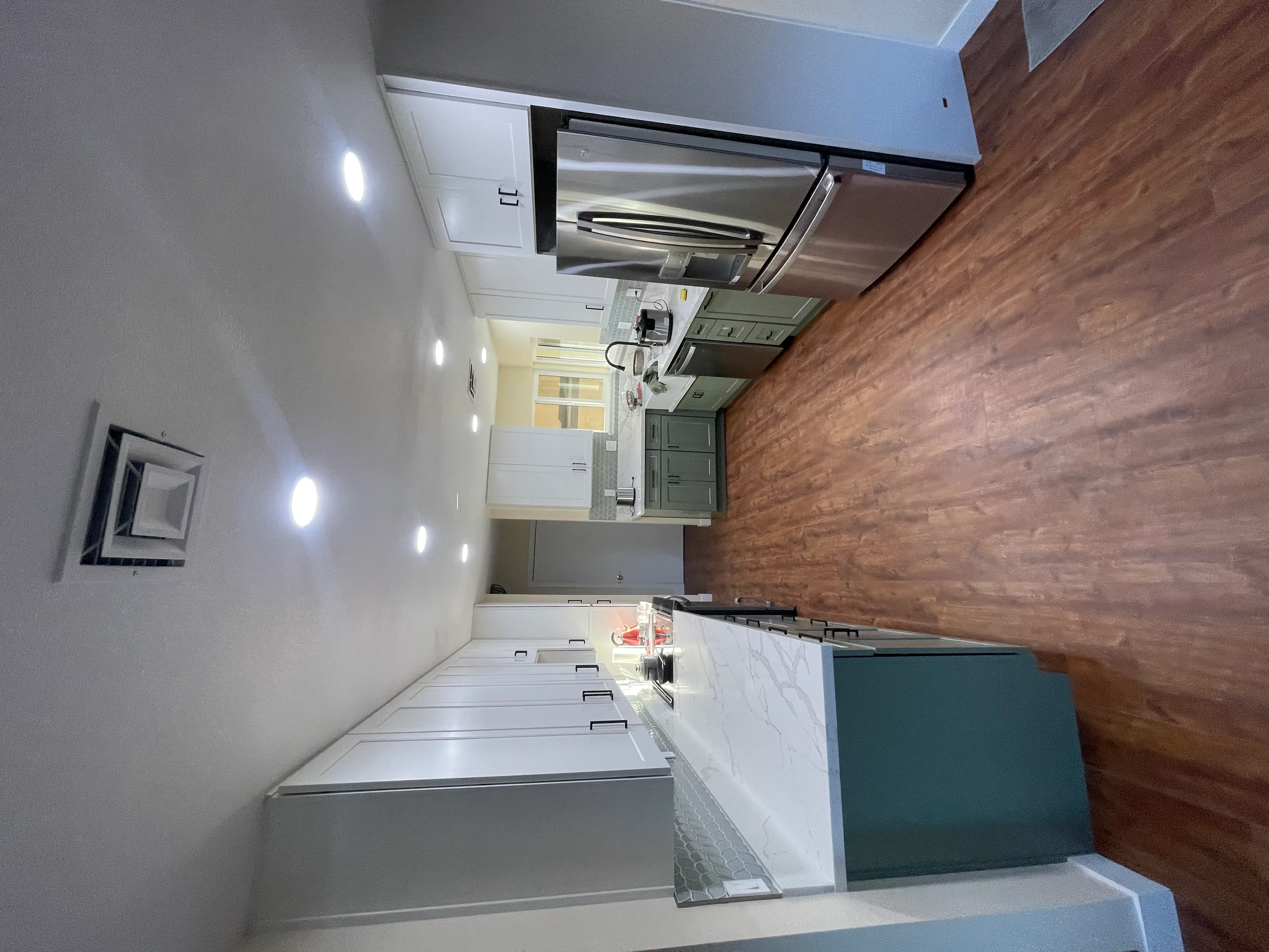 Kitchen remodel with white cabinetry, stainless steel hood, wood-look vinyl flooring, and marble countertops