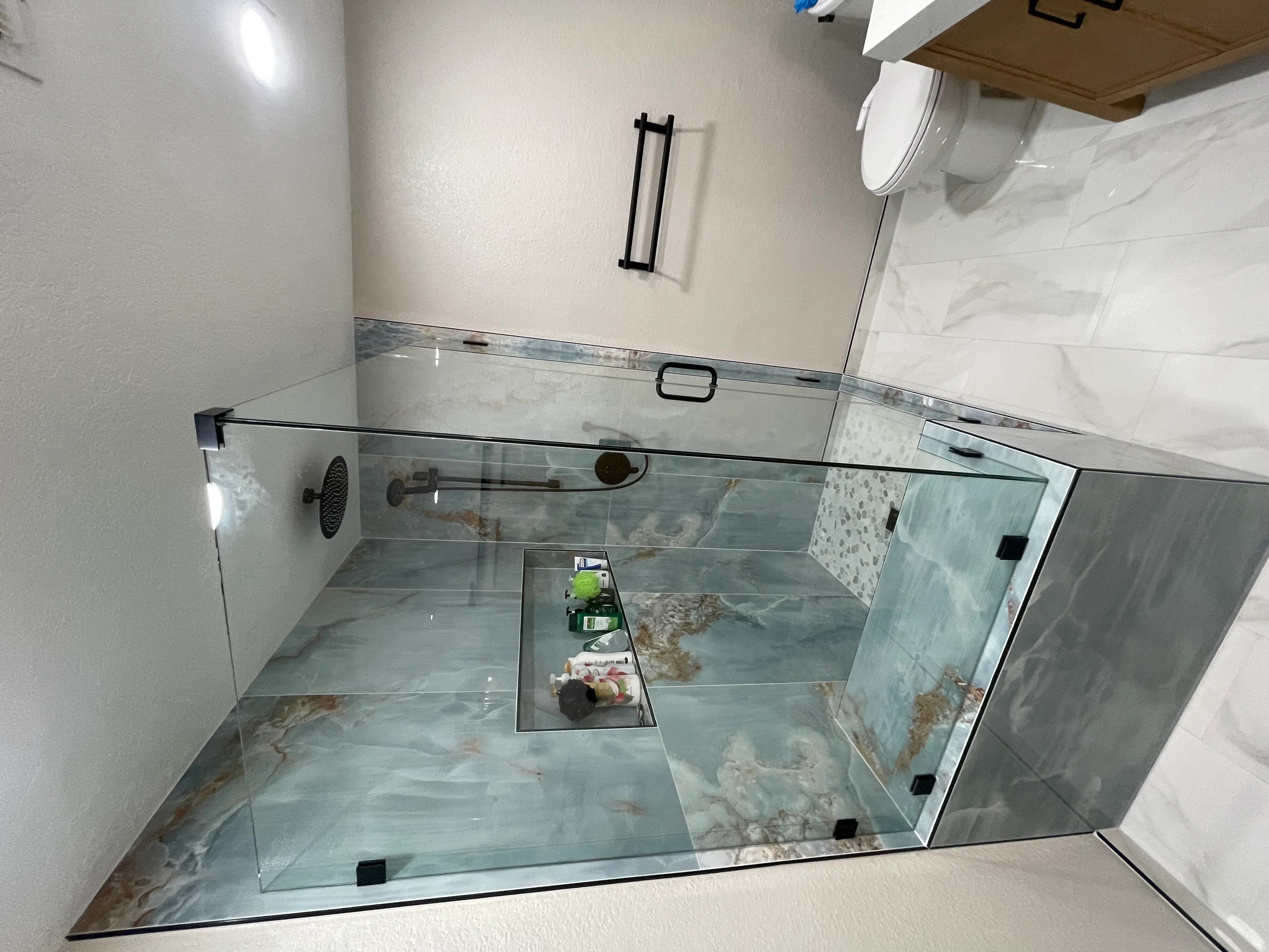 Frameless glass shower with bronze fixtures, marble tile floor, and linear drain