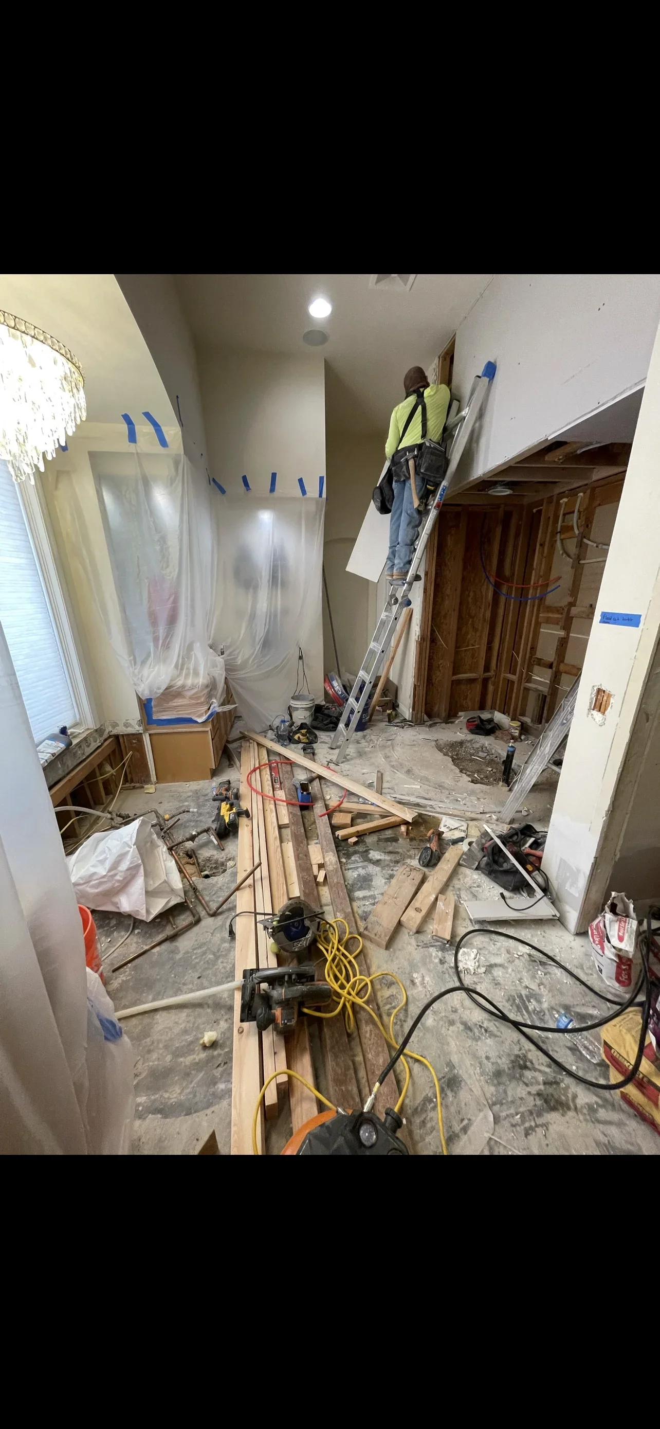 Drywall installation and framing work with protective sheeting, concrete floor, and workers on ladder