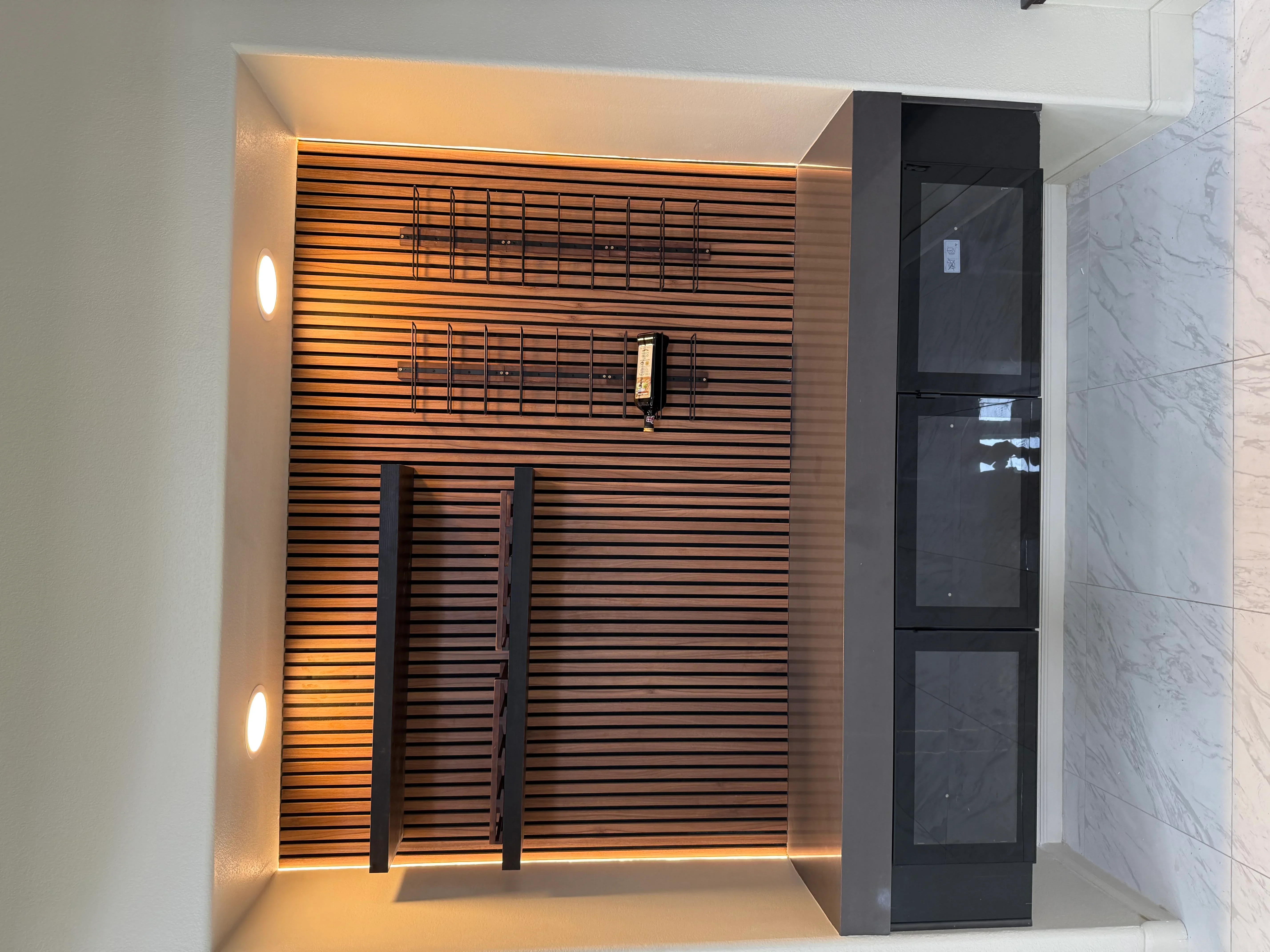 Horizontal wood slat accent wall with warm LED lighting, black towel bars, and glass shower enclosure in modern bathroom