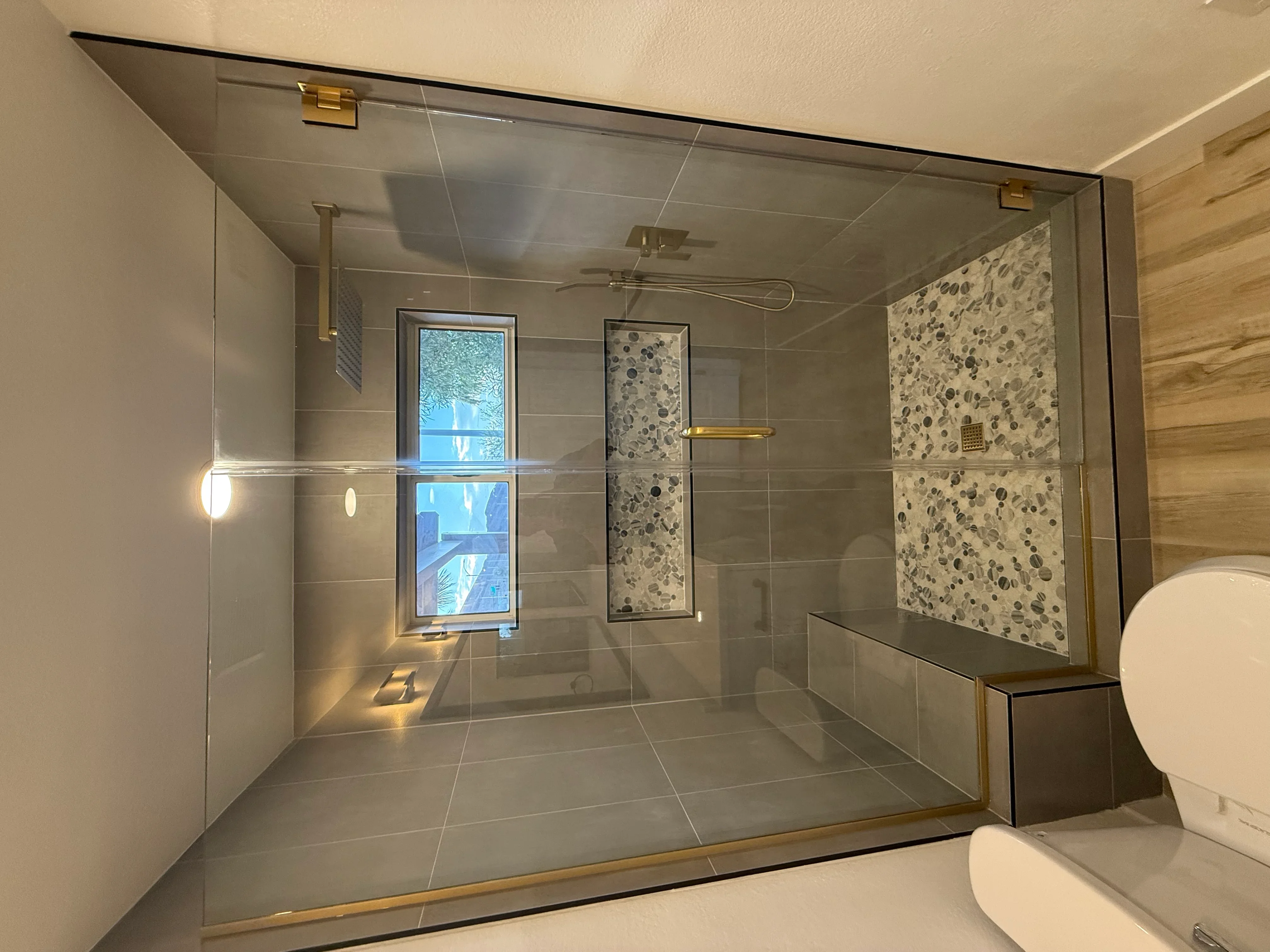 Frameless glass shower with gray tile, mosaic accents, brass fixtures, and rainfall head