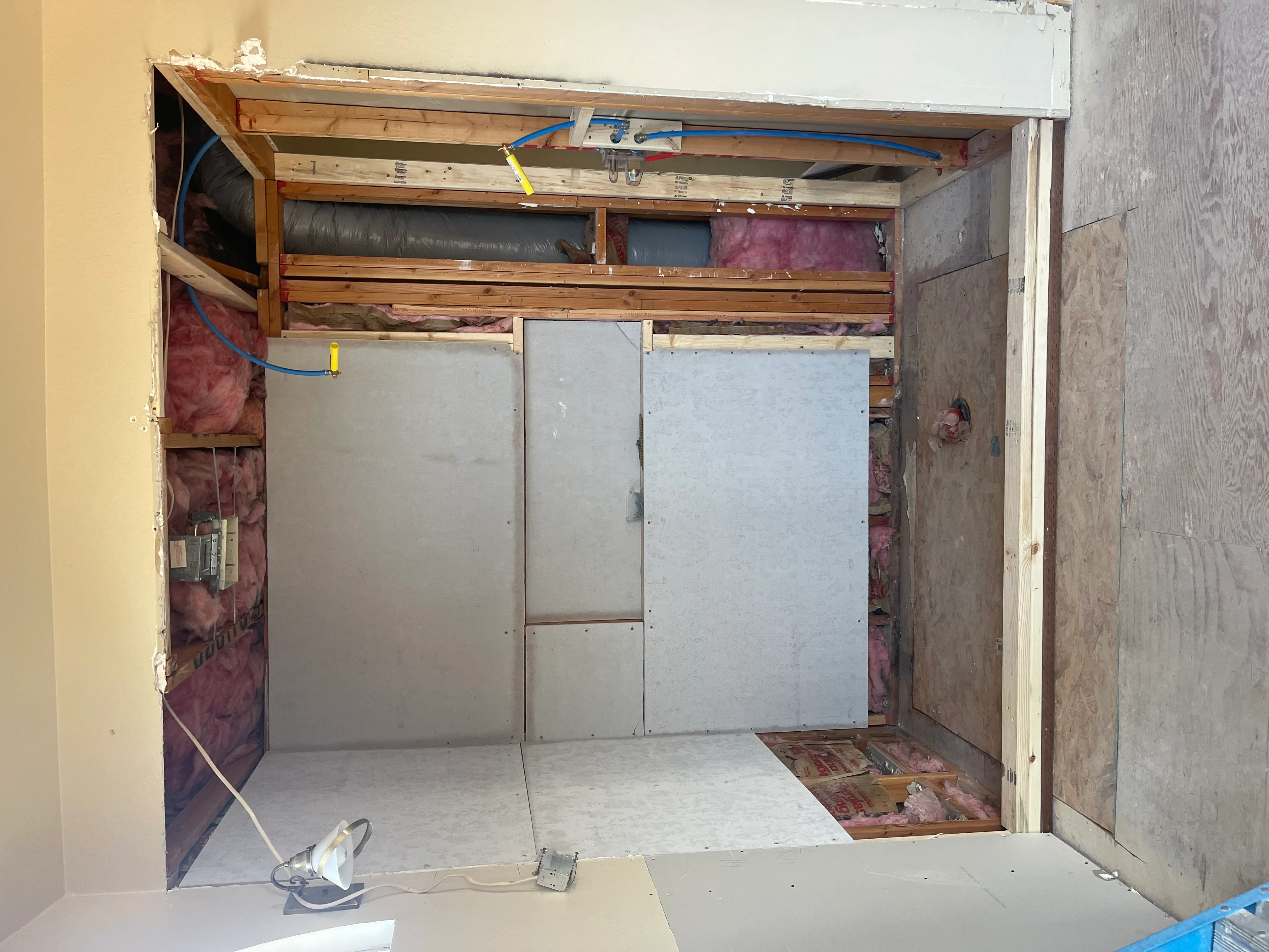 Bathroom framing with wood studs, drywall panels, pink insulation, and electrical conduit during renovation