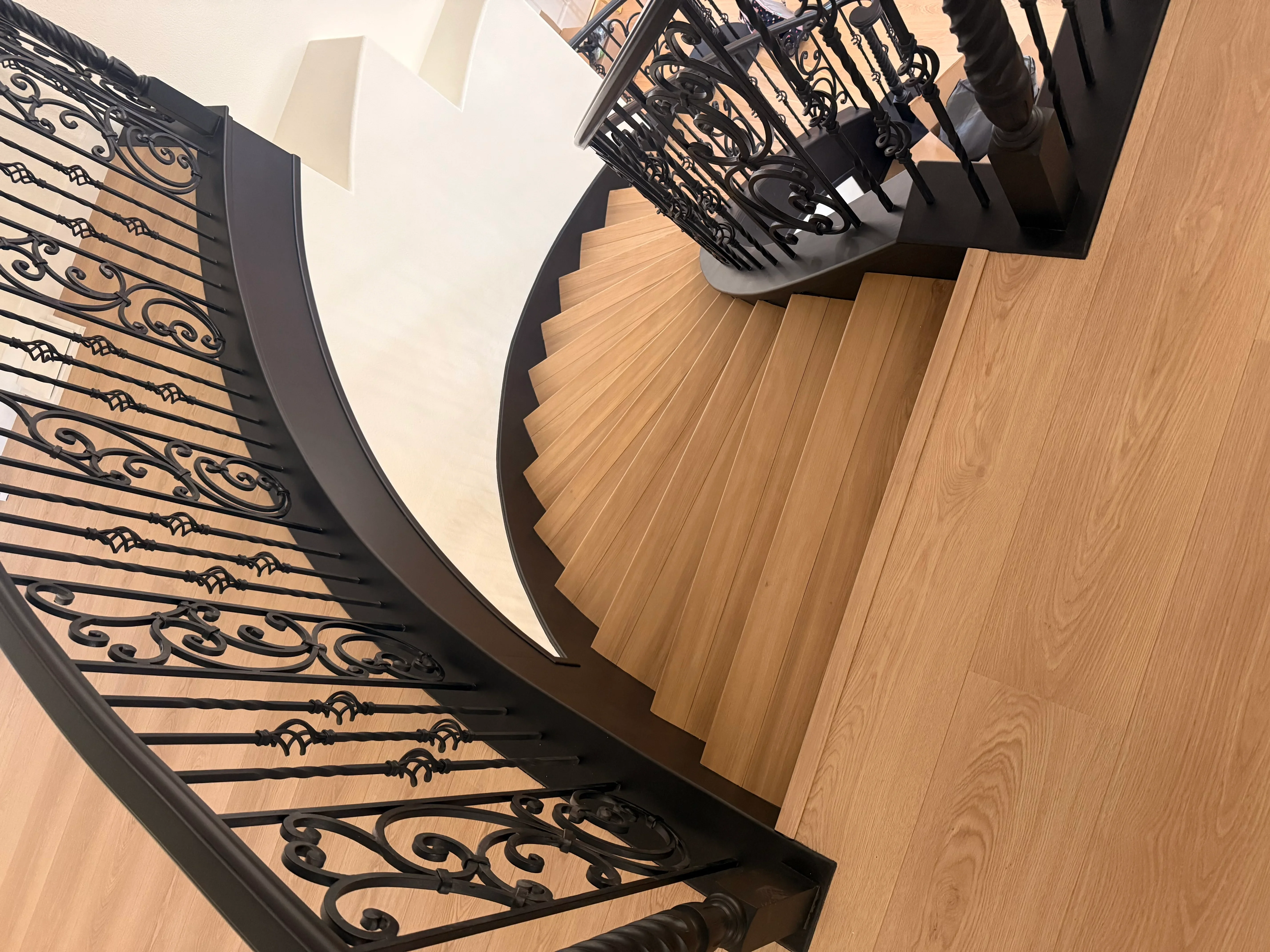 Curved hardwood staircase with black ornamental iron railings and decorative balusters