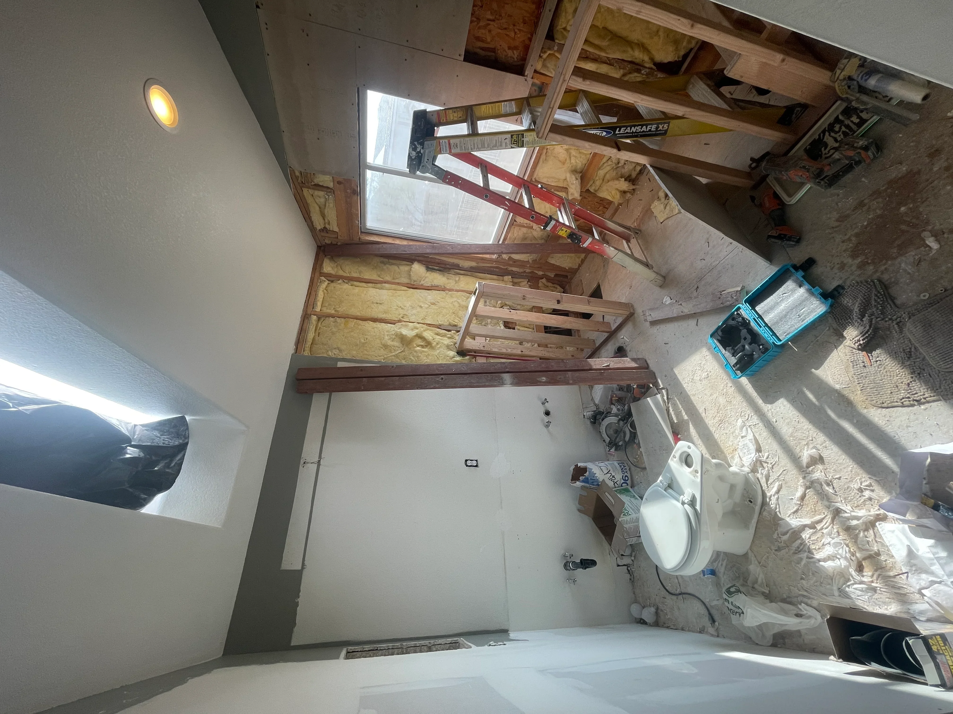 Bathroom renovation in progress with drywall, insulation, recessed lighting, and toilet installation