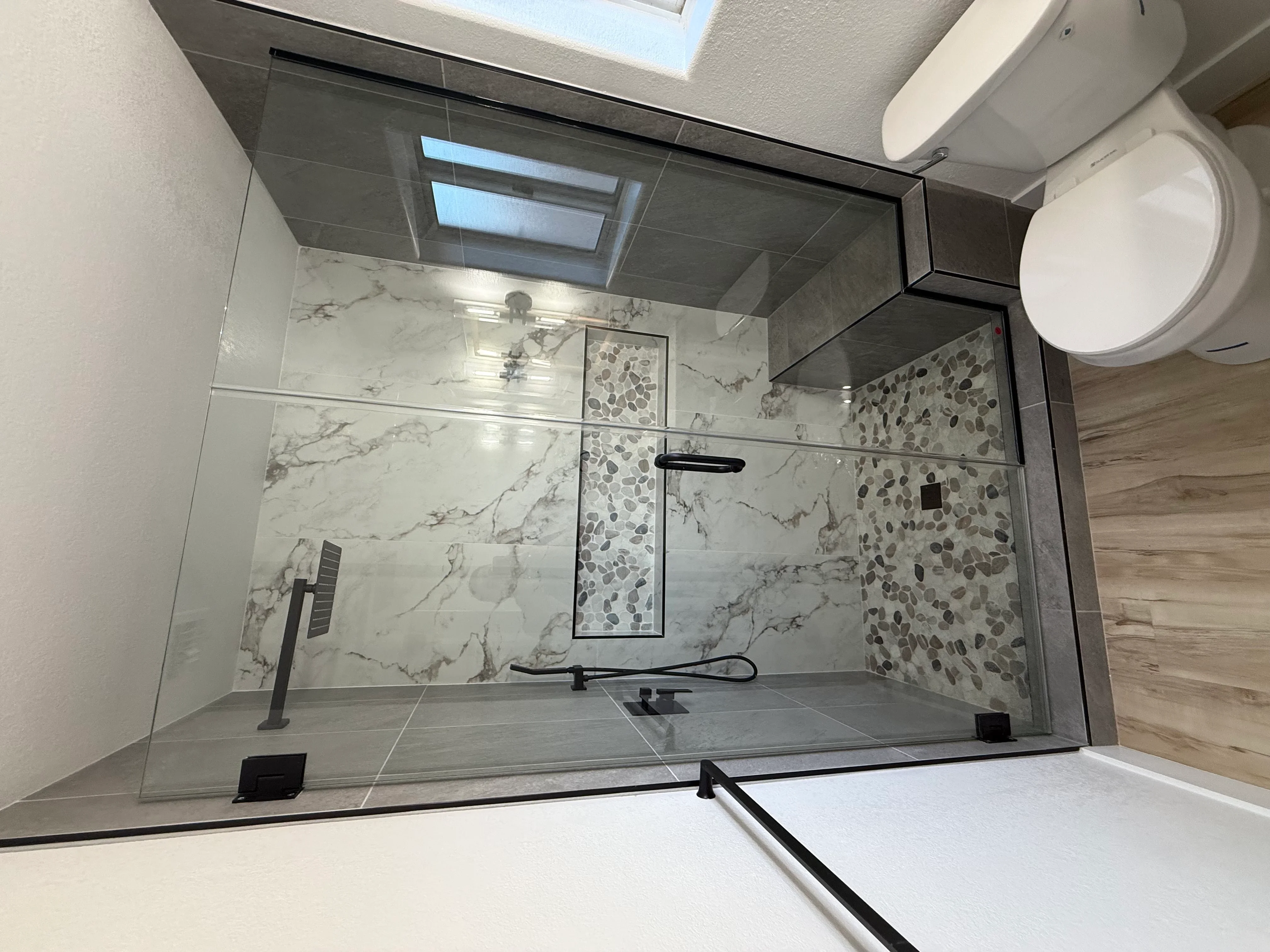 Walk-in shower with marble tile walls, pebble mosaic accent, frameless glass door, and matte black fixtures