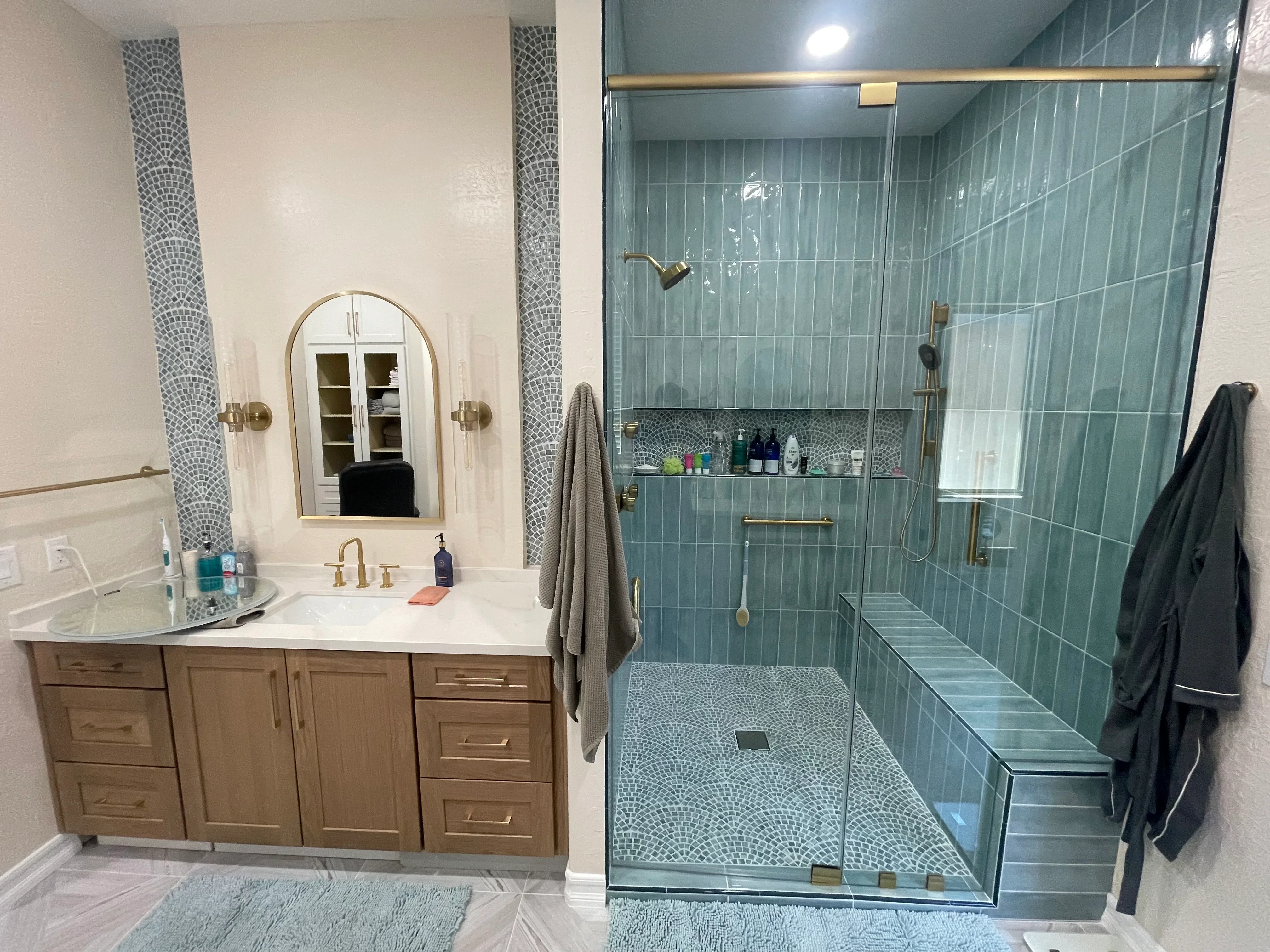 Bathroom with teal subway tile shower, mosaic tile floor, wood vanity, and brass fixtures